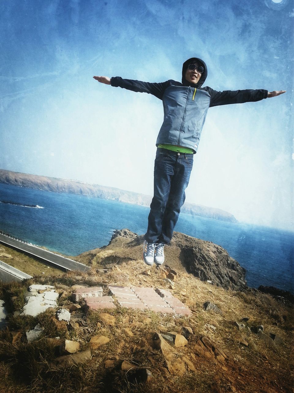 full length, sky, lifestyles, standing, casual clothing, leisure activity, blue, sea, rear view, rock - object, men, cloud - sky, day, water, nature, sunlight, arms outstretched, tranquility