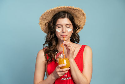 Portrait of a beautiful young woman drinking glass against blue background