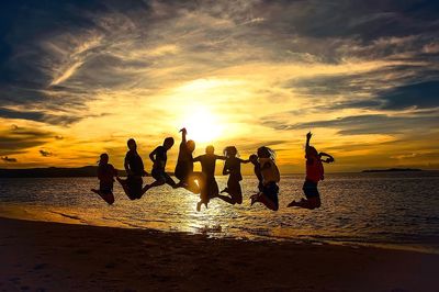 Silhouette people on beach against sky during sunset