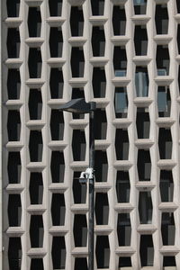 A lamp post and a cctv camera  in front of a facade made of geometric pattern, in paris. 