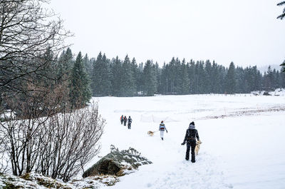 Rear view of people walking on snow covered field