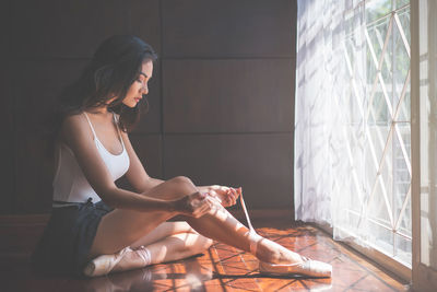 Young woman wearing shoe while sitting on floor