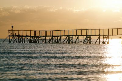 Silhouette pier over sea against sky during sunset