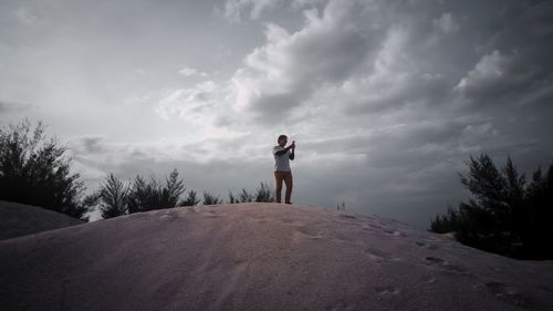 Man using mobile phone while standing on sand against sky