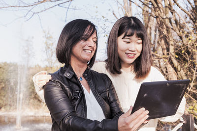 Smiling colleague holding digital tablet standing at park