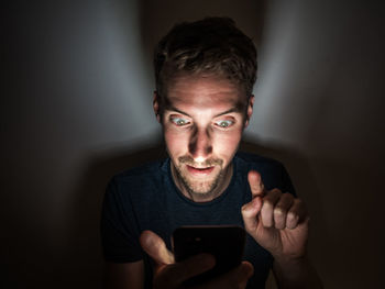 Young man using phone while sitting in darkroom