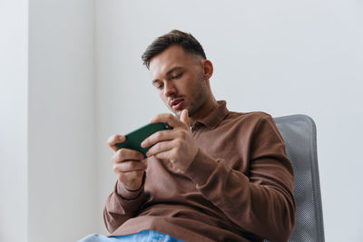 Portrait of young man sitting on sofa against white background