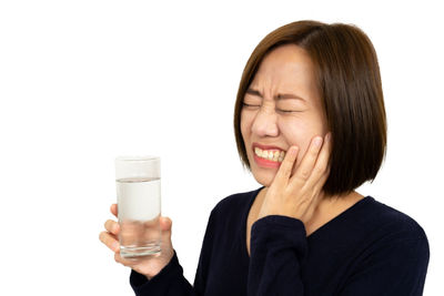 Portrait of a young woman drinking glass against white background