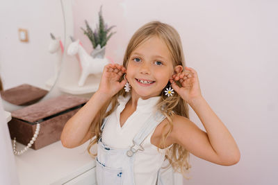 Happy child, a seven-year-old girl, tries on her mother's earrings with a wide smile