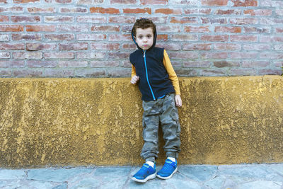 Boy in hooded sweatshirt and camouflage pants leaning against brick wall