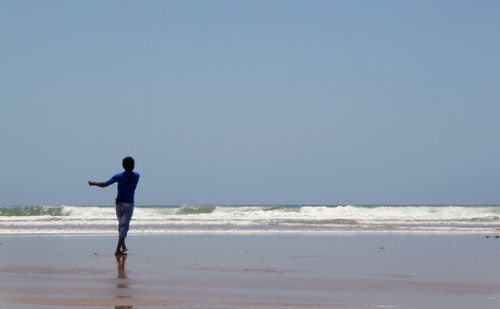 Rear view of man standing at beach against clear blue sky