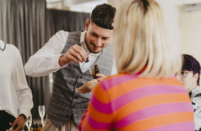 Smiling businessman giving sample of essential oil to colleague during event at convention center