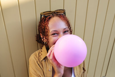 Happy woman blowing bubble gum in front of wall