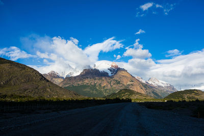 Road amidst snowcapped mountains against blue sky