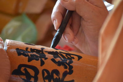Cropped image of craftsperson writing script on bamboo decor at workshop