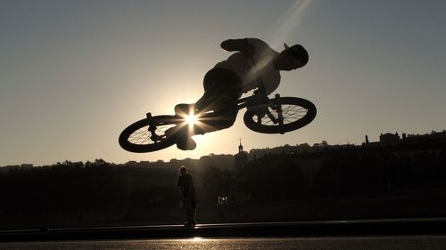 Low angle view of man jumping with bicycle on street during sunset