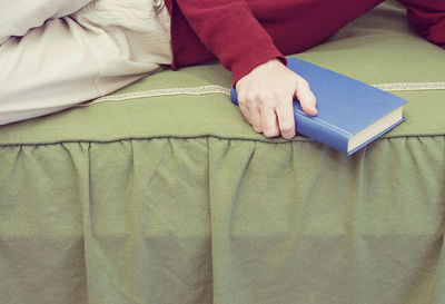 Midsection of man holding book while lying on sofa at home