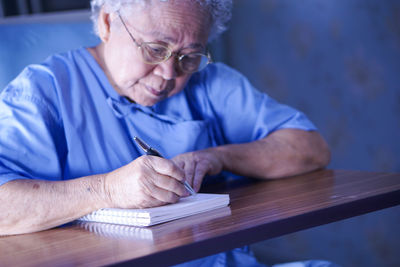 Senior man writing in book on desk at home