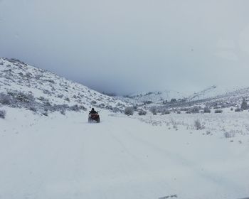 Rear view of person walking on snow covered mountain against sky