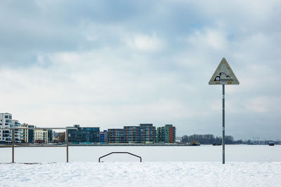 Road sign in city against sky during winter