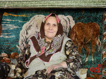 Portrait of senior woman sitting against paintings on wall