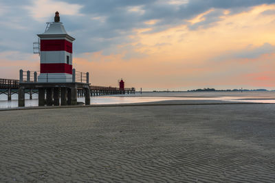 Lighthouse on beach against sky during sunset