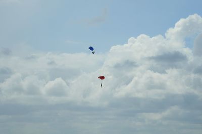 Low angle view of people paragliding against sky