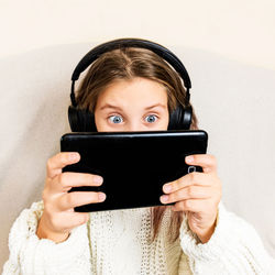 Child girl sits in wireless headphones and looks into a digital tablet with surprise ,gadgets, 