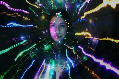 Woman seen through illuminated lighting equipment against black background