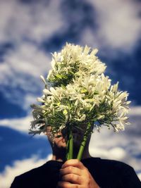 Close-up of man holding bouquet of white flowers against cloudy sky.