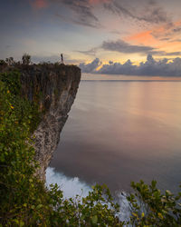 Scenic view of sea with woman standing on mountain against sky during sunset