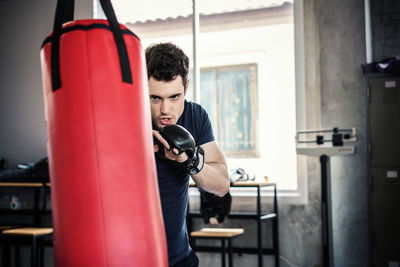 Handsome man in boxing gloves punching bags exercise in fitness gym.