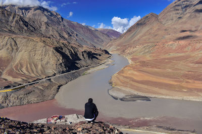Rear view of man crouching on mountain by river