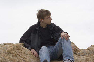 Teenage boy sitting on rocks against clear sky