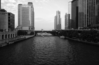 Bridge over river amidst buildings in city against sky
