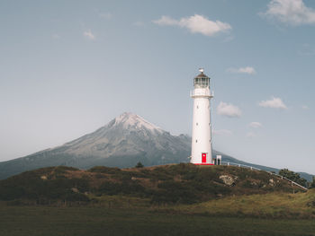 Lighthouse by mountain against sky