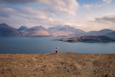 Young girl standing by lake against highland scenery 