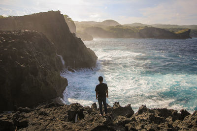 Rear view of man standing on rock by sea