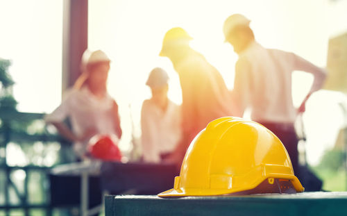 Close-up of hardhat on table with coworkers discussing in background