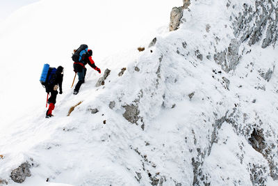 Low angle view of mountaineers climbing snowcapped mountain against sky
