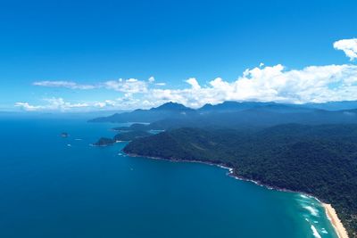 Aerial view of sea and mountains against blue sky