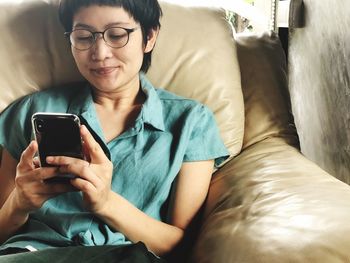 Close-up of smiling man using mobile phone while sitting on sofa