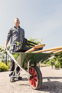 Low angle view of man holding wheelbarrow at community garden