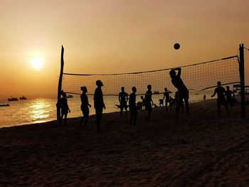 Silhouette people playing soccer on beach against sky during sunset