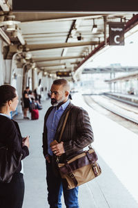 Coworkers talking while standing at railroad station platform during business travel