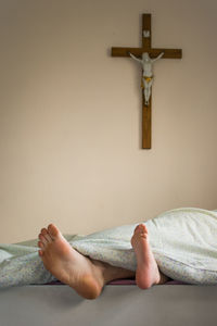 Low section of person by cross on wall lying down at bed