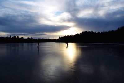 Silhouette people playing ice hockey against sky during sunset