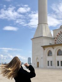 Woman photographing with mobile phone against sky