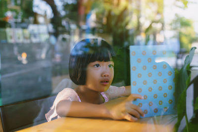 Cute girl reading book on table seen through glass