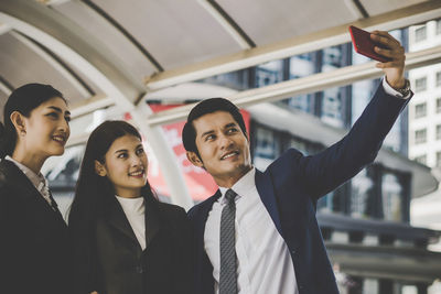 Smiling business people taking selfie with mobile phone while standing in office